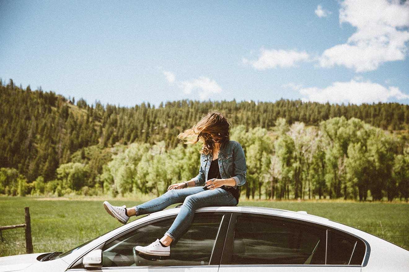 Frau sitzt auf Auto in der Natur